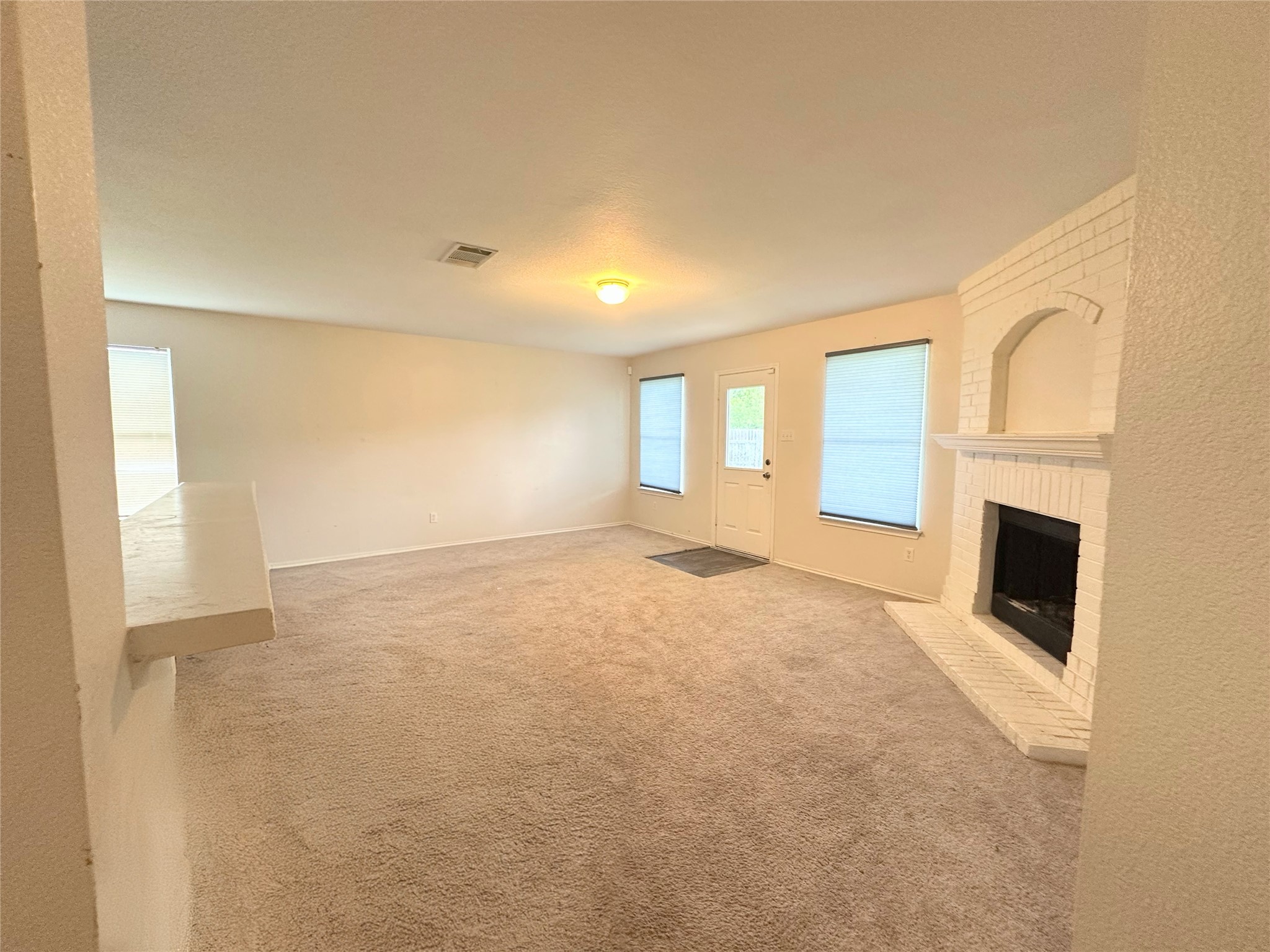 12929 Waynespur Lane Elgin, TX 78621 - Photo 7 of 20 Living area with light-colored carpet, a white brick fireplace, and windows with blinds