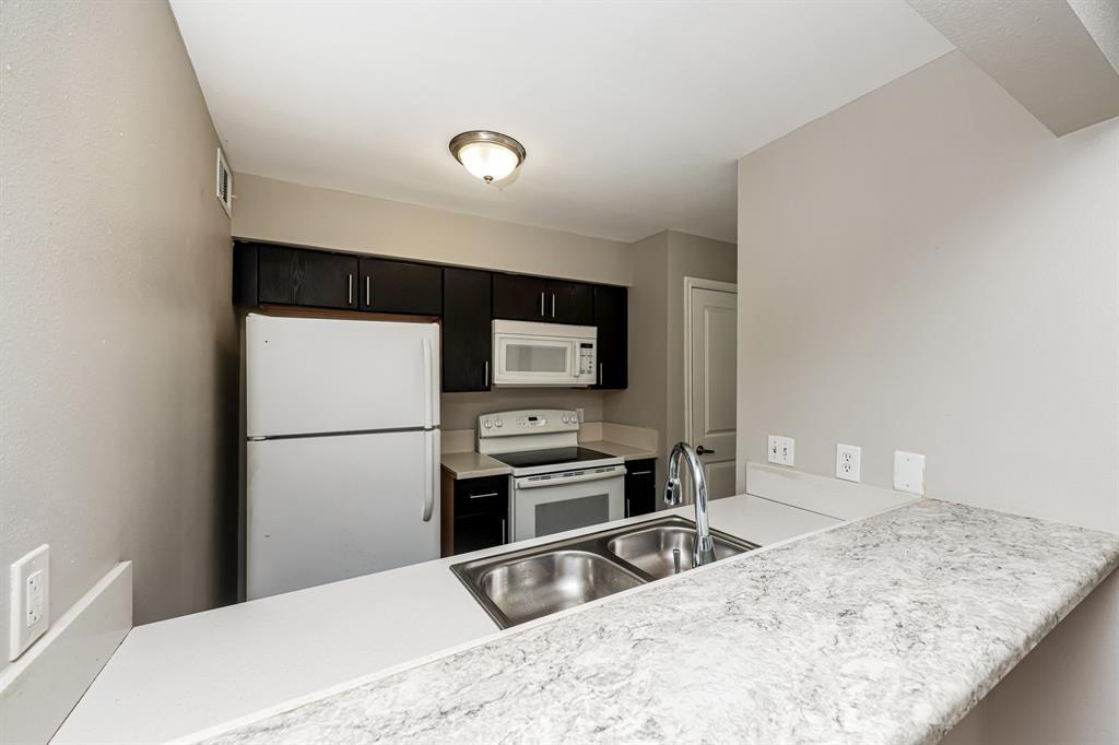 4622 Monarch Street, Unit 202 Dallas, TX 75204 - Photo 10 of 16 Kitchen featuring dark cabinetry, white appliances, a double basin stainless steel sink, a modern faucet, and light-toned countertops