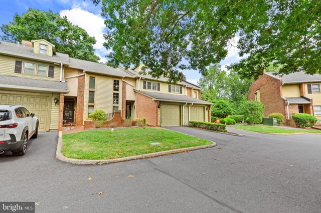 a view of a white house in front of a yard with plants and large tree