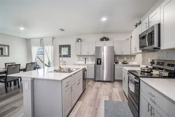a kitchen with stainless steel appliances granite countertop a stove top oven a sink a refrigerator and white cabinets