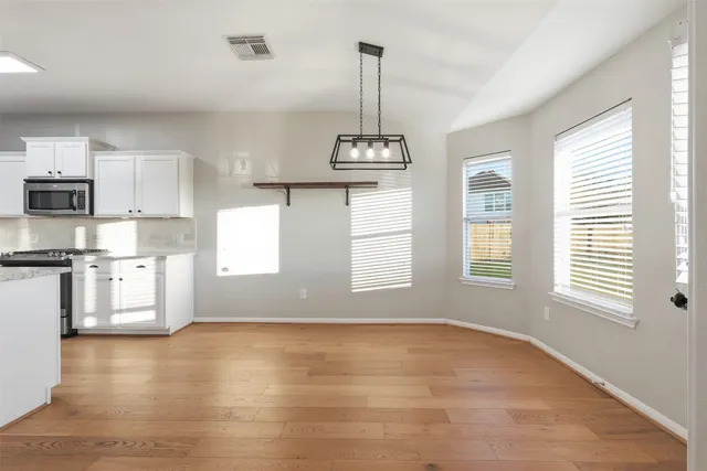 a view of kitchen with stainless steel appliances granite countertop a stove a sink a refrigerator white cabinets and wooden floor