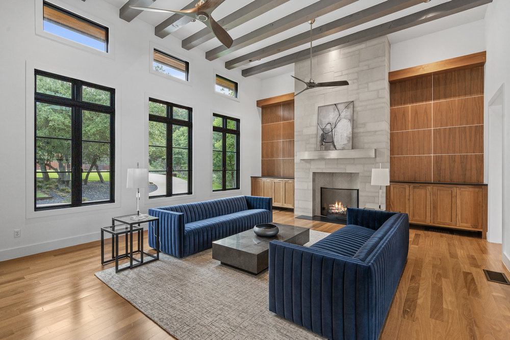 1905 Paisano Road Austin, TX 78746 - Photo 16 of 40 A spacious living area showcasing warm wood flooring, a stone fireplace, and ample natural illumination.