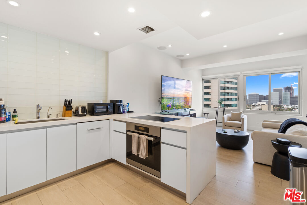 10501 Wilshire Boulevard, Unit 1605 Los Angeles, CA 90024 - Photo 24 of 27 a kitchen with sink a stove and white cabinets