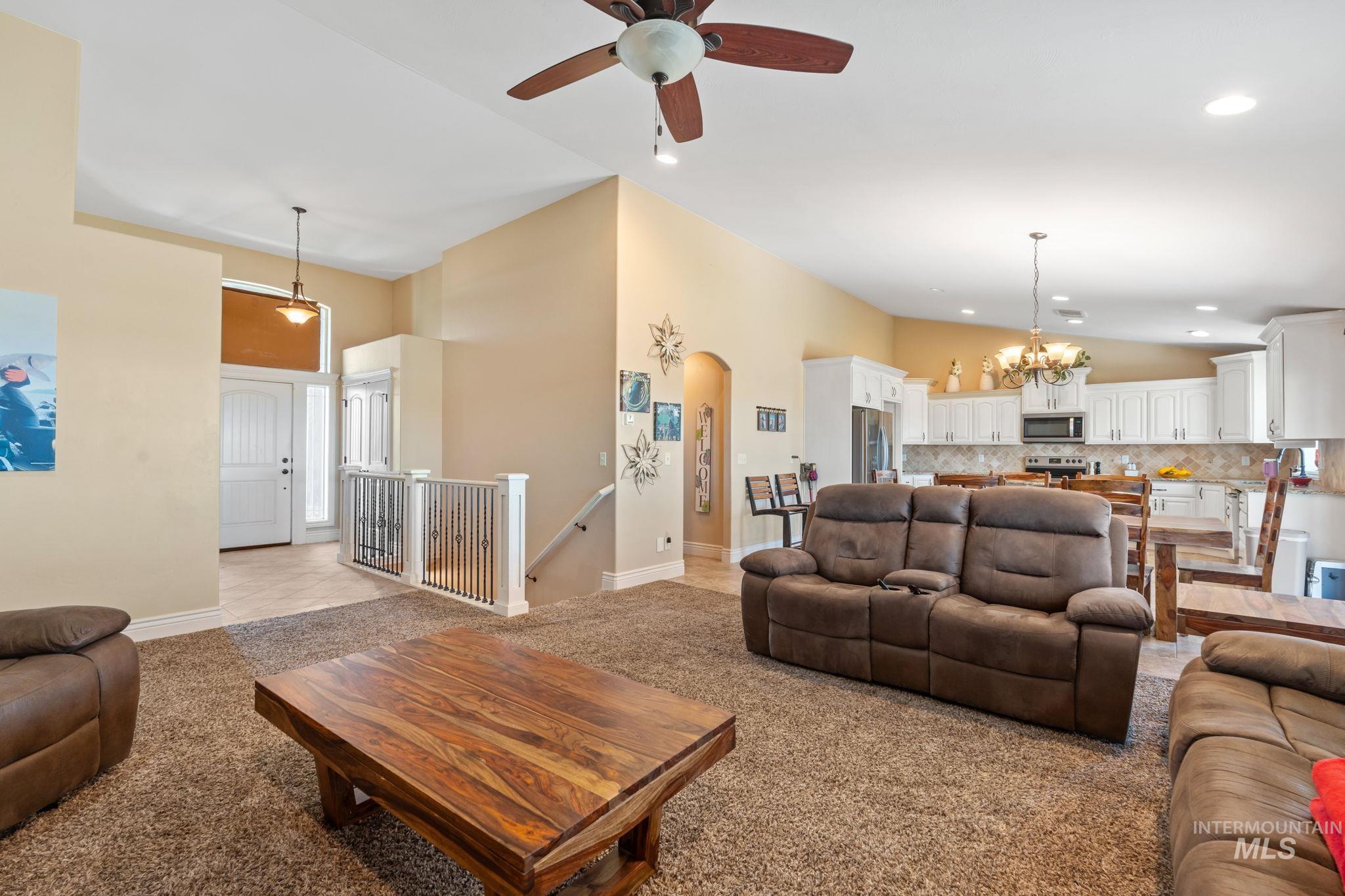 3625 North 2000 West Rexburg, ID 83440 - Photo 48 of 50 Living room featuring arched walkways, a ceiling fan, light carpet, vaulted ceiling, and a chandelier