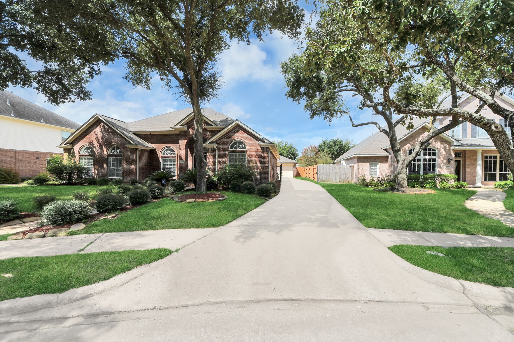5815 Pheasant Ridge Lane Houston, TX 77041 - Photo 3 of 46 Charming brick home with elegant arched windows, nestled among mature trees and lush landscaping, featuring a wide driveway leading to a detached garage.