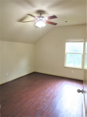 an empty room with wooden floor chandelier fan and windows