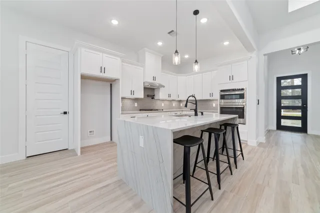 a large white kitchen with kitchen island a large counter space a sink stainless steel appliances and cabinets