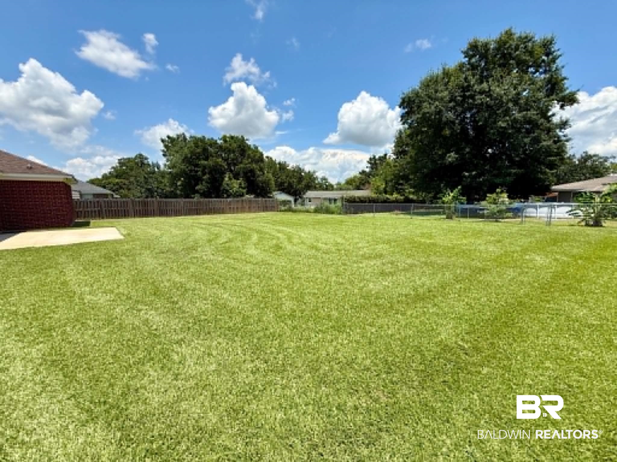 123 Pennbrooke Loop Foley, AL 36535 - Photo 13 of 49 Expansive green lawn with mature perimeter trees, a solid wood privacy fence, and a concrete patio pad