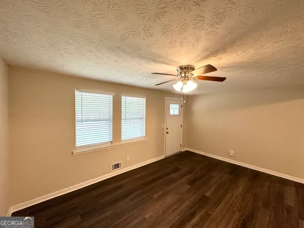 an empty room with wooden floor fan and windows