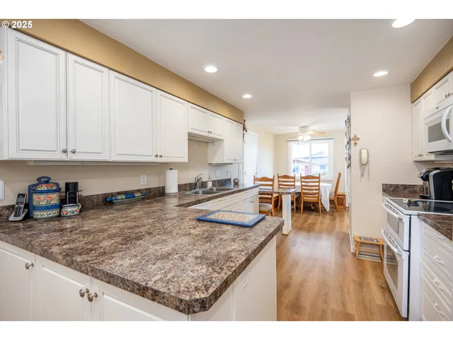 a kitchen with stainless steel appliances granite countertop a stove top oven a sink a dining table and chairs with wooden floor