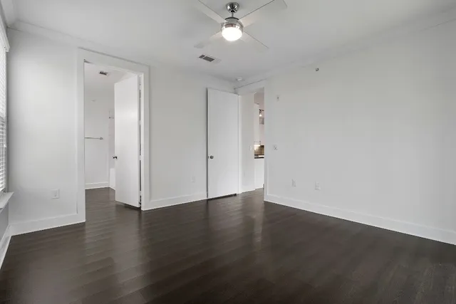 a view of an empty room with wooden floor and a ceiling fan