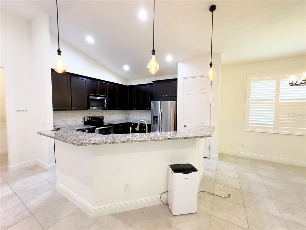 3775 Manorwood Loop Parrish, FL 34219 - Photo 8 of 30 a kitchen with stainless steel appliances granite countertop a sink a stove a refrigerator and chairs with wooden floor