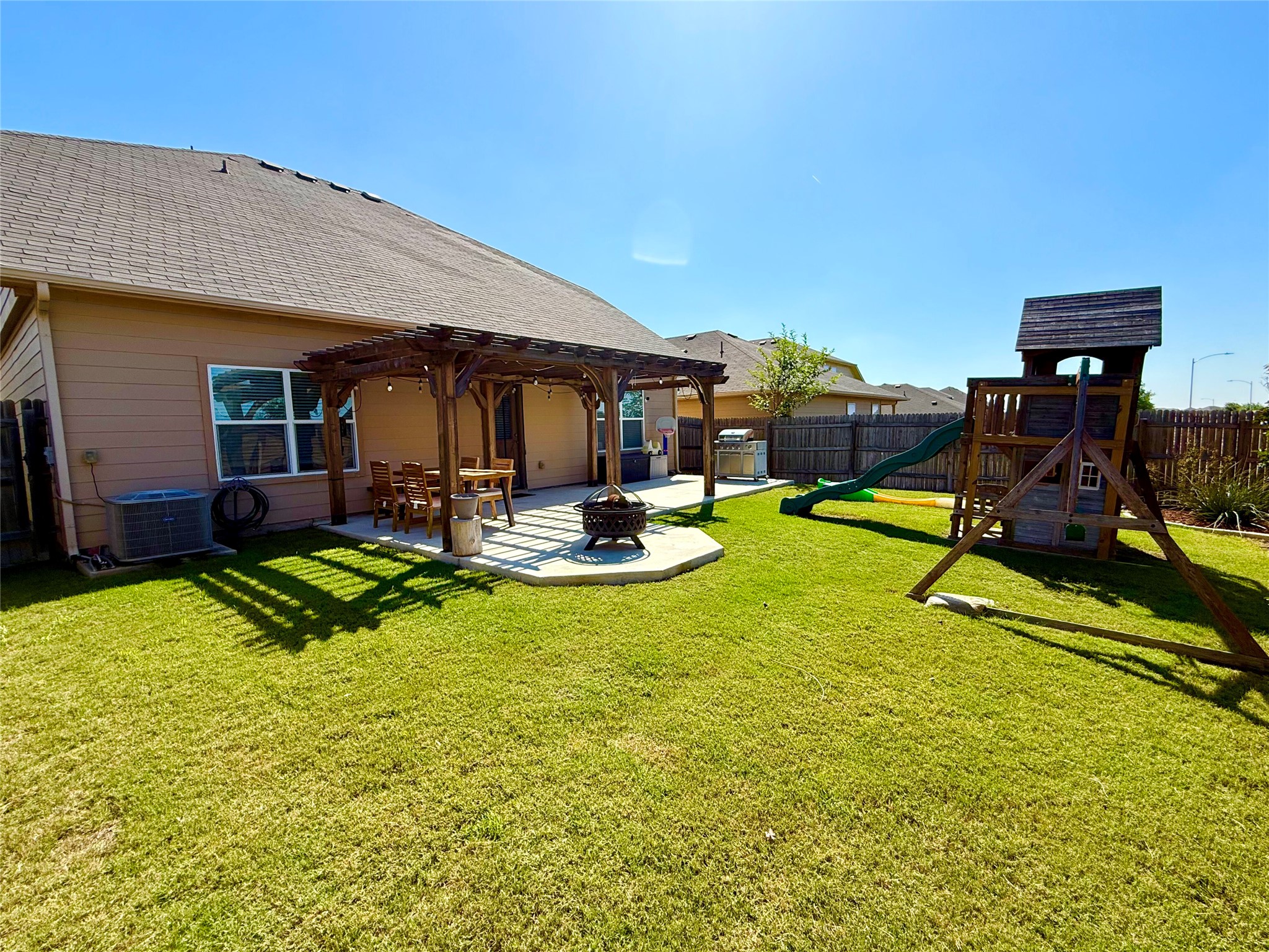 11700 Andesite Road Manor, TX 78653 - Photo 29 of 32 A spacious backyard retreat features a pergola-covered patio, fire pit, and a children's play set.