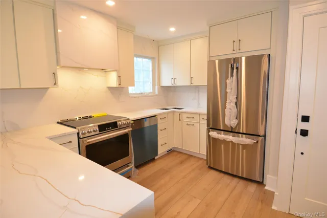 a kitchen with stainless steel appliances granite countertop a refrigerator a sink dishwasher a stove and white countertops with wooden floor