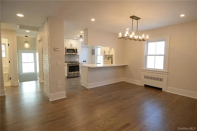 an empty room with wooden floor and kitchen view