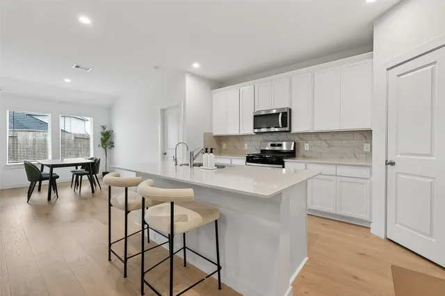 a kitchen with stainless steel appliances a stove a sink a microwave a dining table and chairs