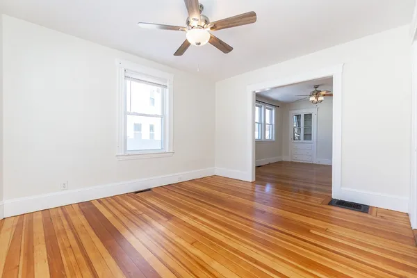 an empty room with wooden floor chandelier fan and windows