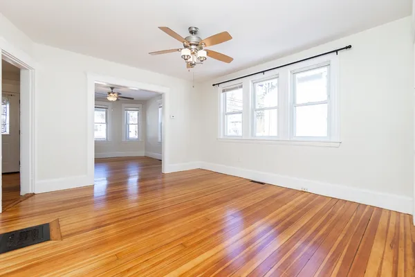 an empty room with wooden floor chandelier fan and windows