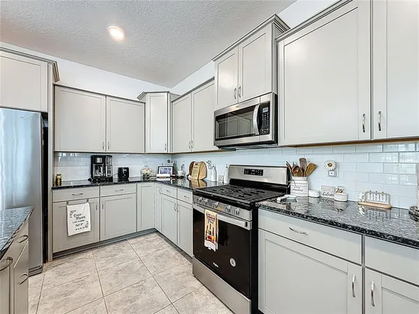 a kitchen with stainless steel appliances granite countertop a stove top oven a refrigerator a sink and white cabinets