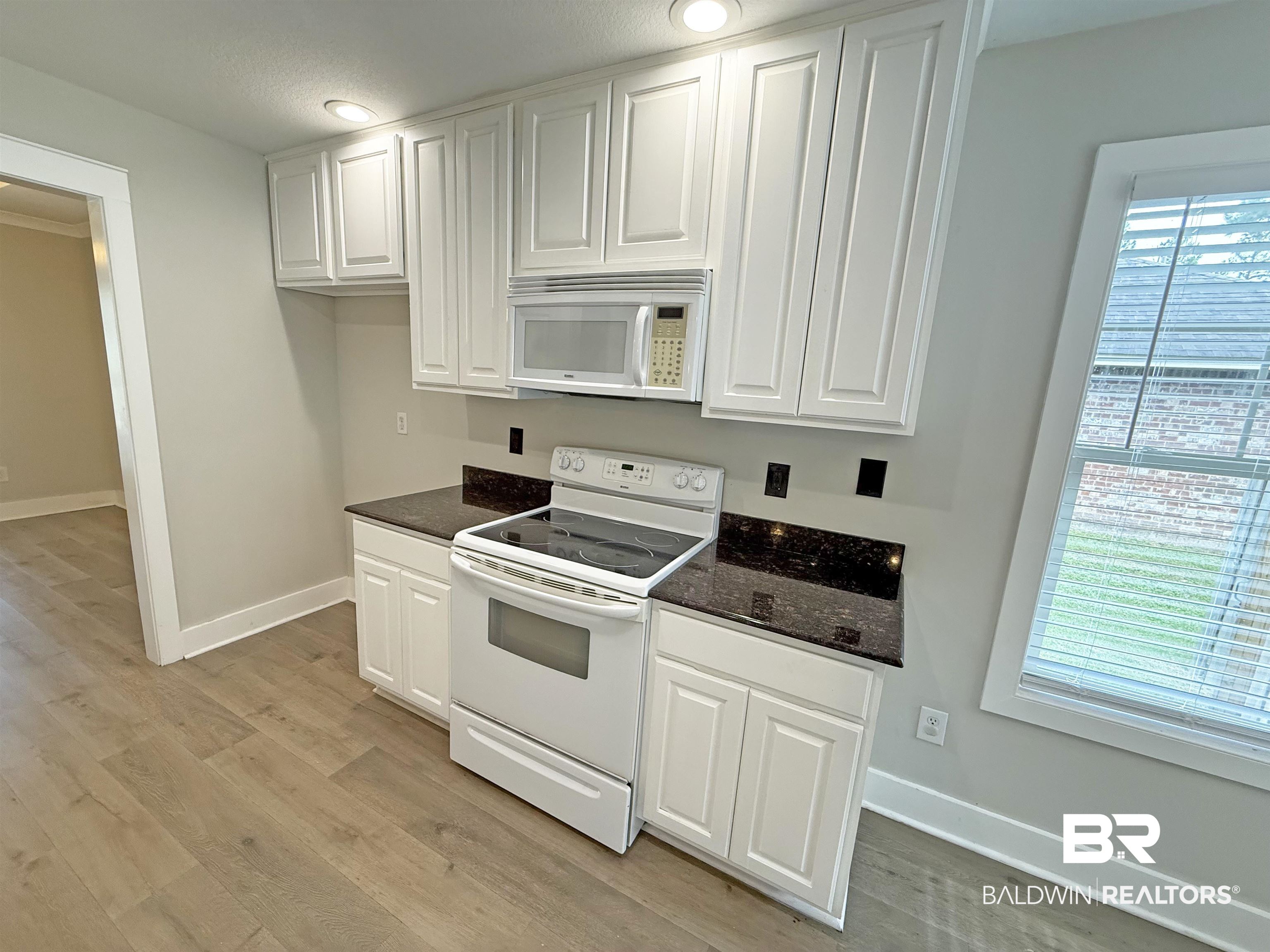 22023 Garland Loop Silverhill, AL 36576 - Photo 12 of 33 Kitchen featuring white appliances, white cabinetry, light wood-style floors, and dark stone countertops