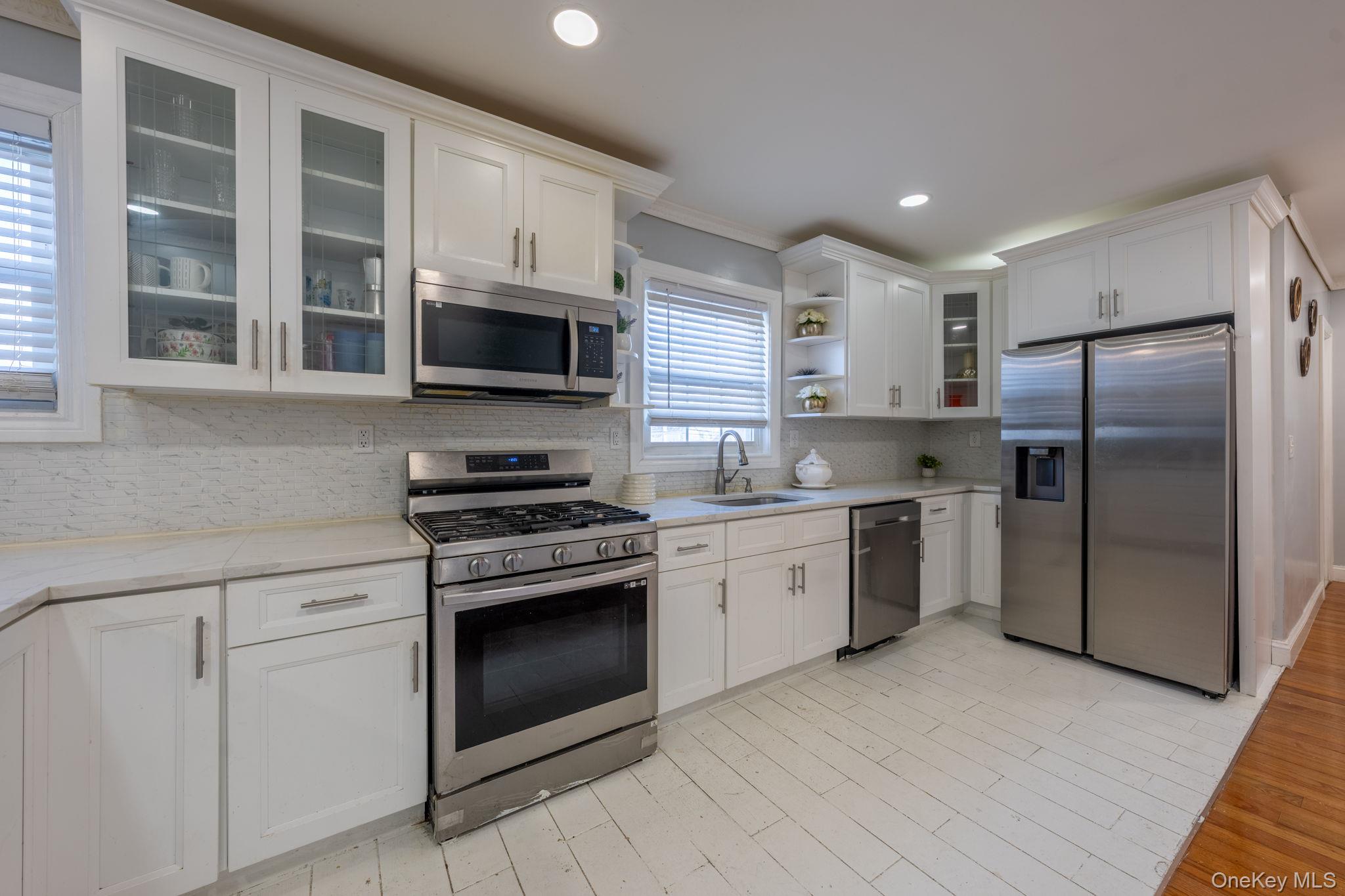 116-01 221st Street Queens, NY 11411 - Photo 7 of 19 Kitchen with glass insert cabinets, open shelves, stainless steel appliances, white cabinets, and light stone counters