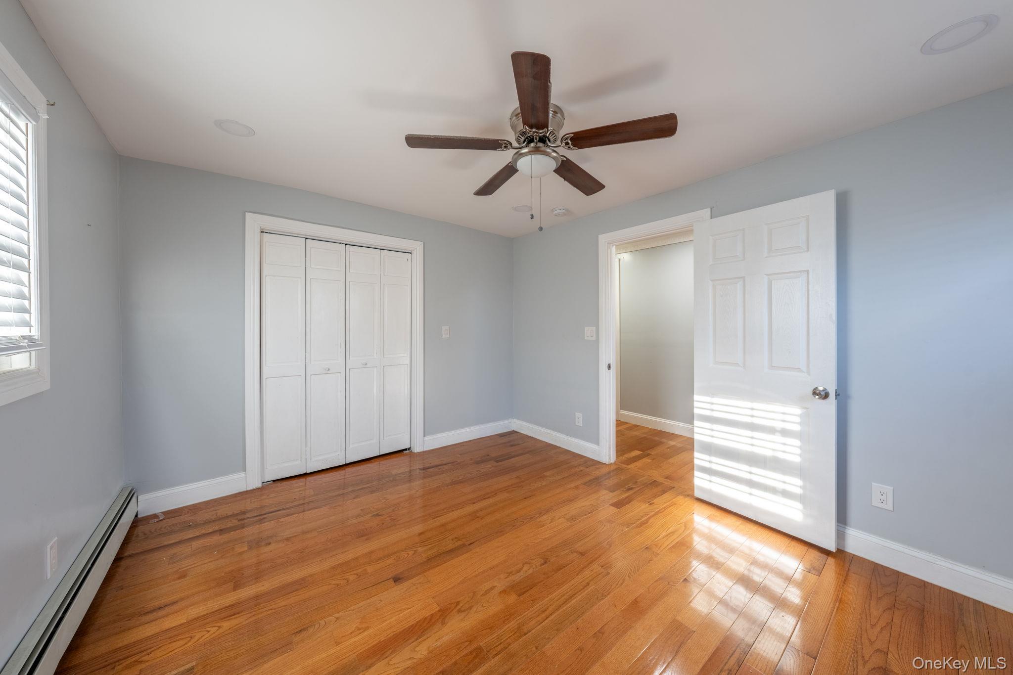 116-01 221st Street Queens, NY 11411 - Photo 9 of 19 Unfurnished bedroom featuring a baseboard heating unit, light wood finished floors, a ceiling fan, and a closet