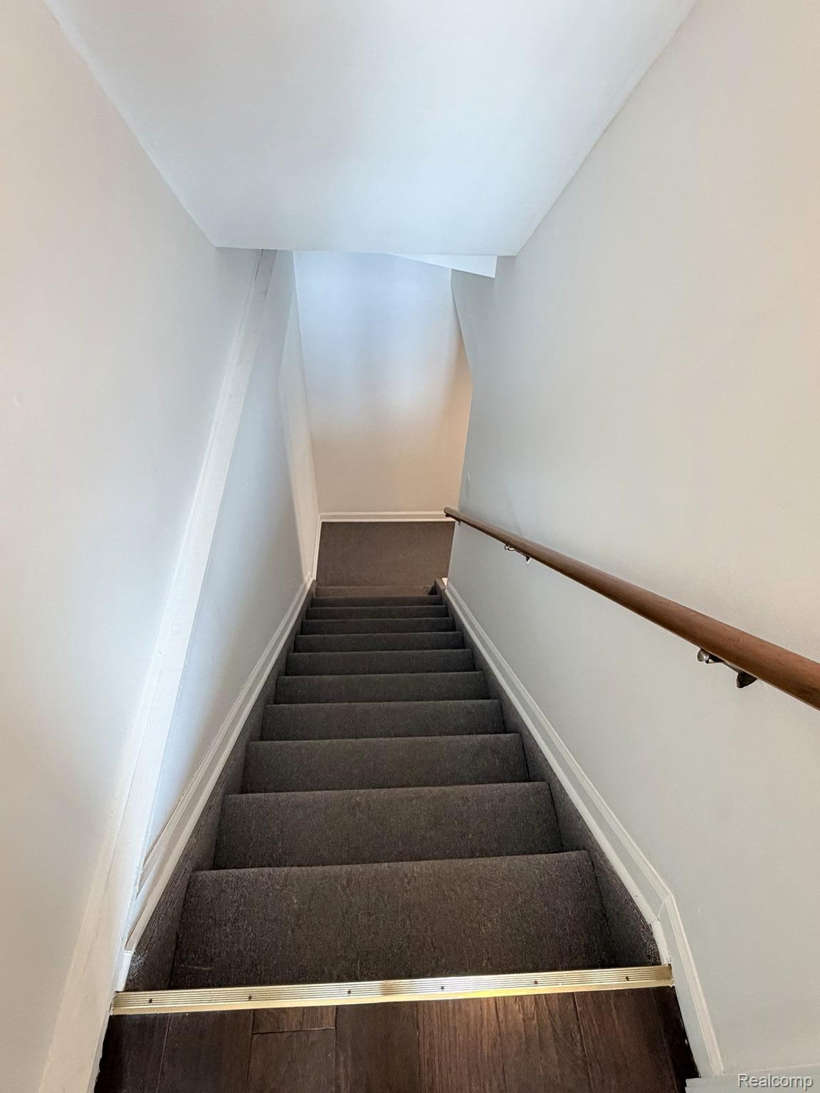 2070 Winchester Road Rochester, MI 48307 - Photo 15 of 34 Carpeted staircase with wood handrail, white wall finishes, and wood-finish flooring at the base