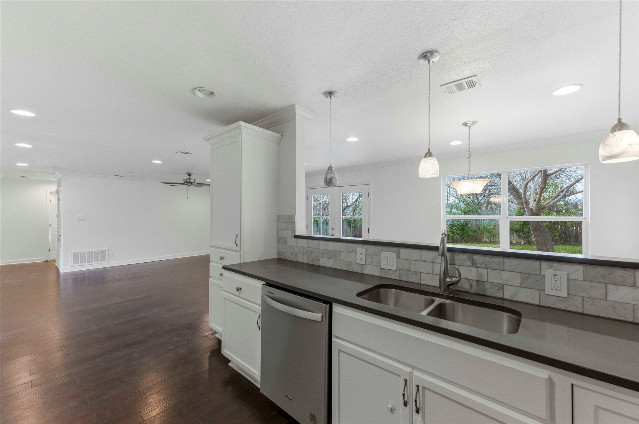 1909 Crooked Lane Austin, TX 78741 - Photo 3 of 25 Kitchen with stainless steel dishwasher, white cabinets, hanging light fixtures, dark wood-type flooring, and backsplash
