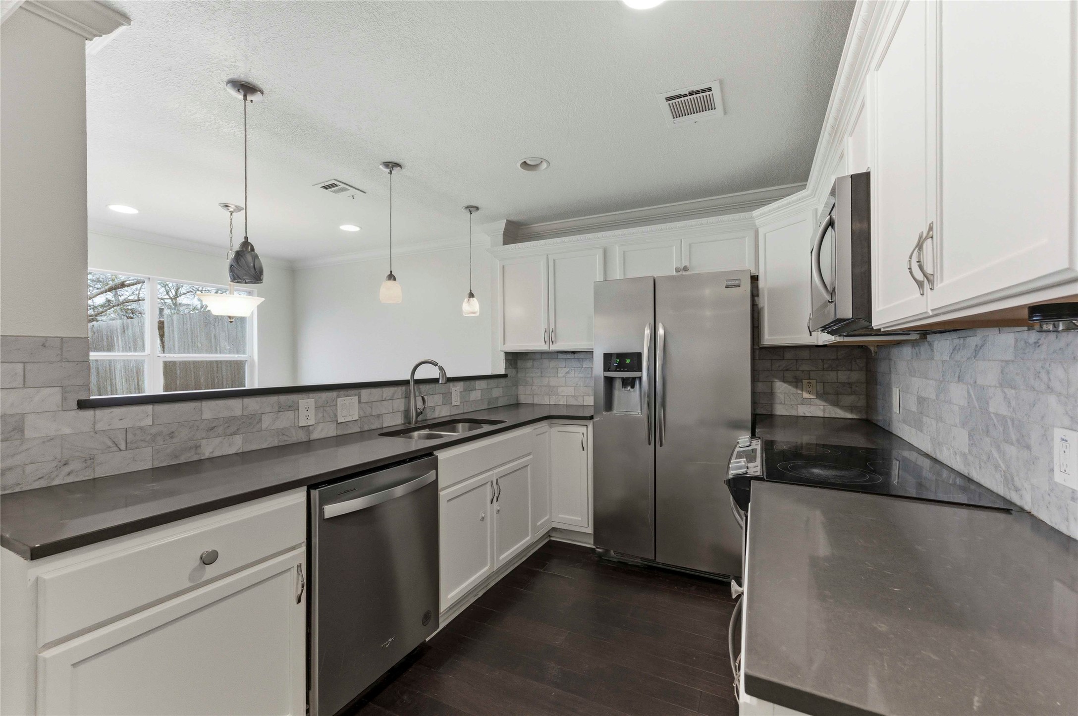 1909 Crooked Lane Austin, TX 78741 - Photo 8 of 25 Kitchen with white cabinets, appliances with stainless steel finishes, pendant lighting, dark wood-style flooring, and backsplash