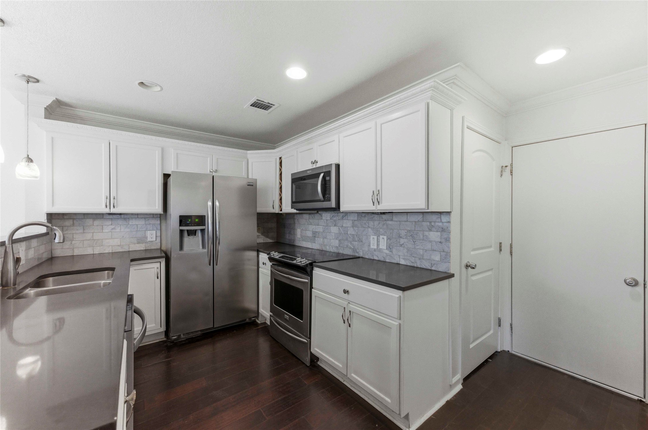 1909 Crooked Lane Austin, TX 78741 - Photo 9 of 25 Kitchen featuring pendant lighting, ornamental molding, stainless steel appliances, white cabinets, and dark wood-type flooring