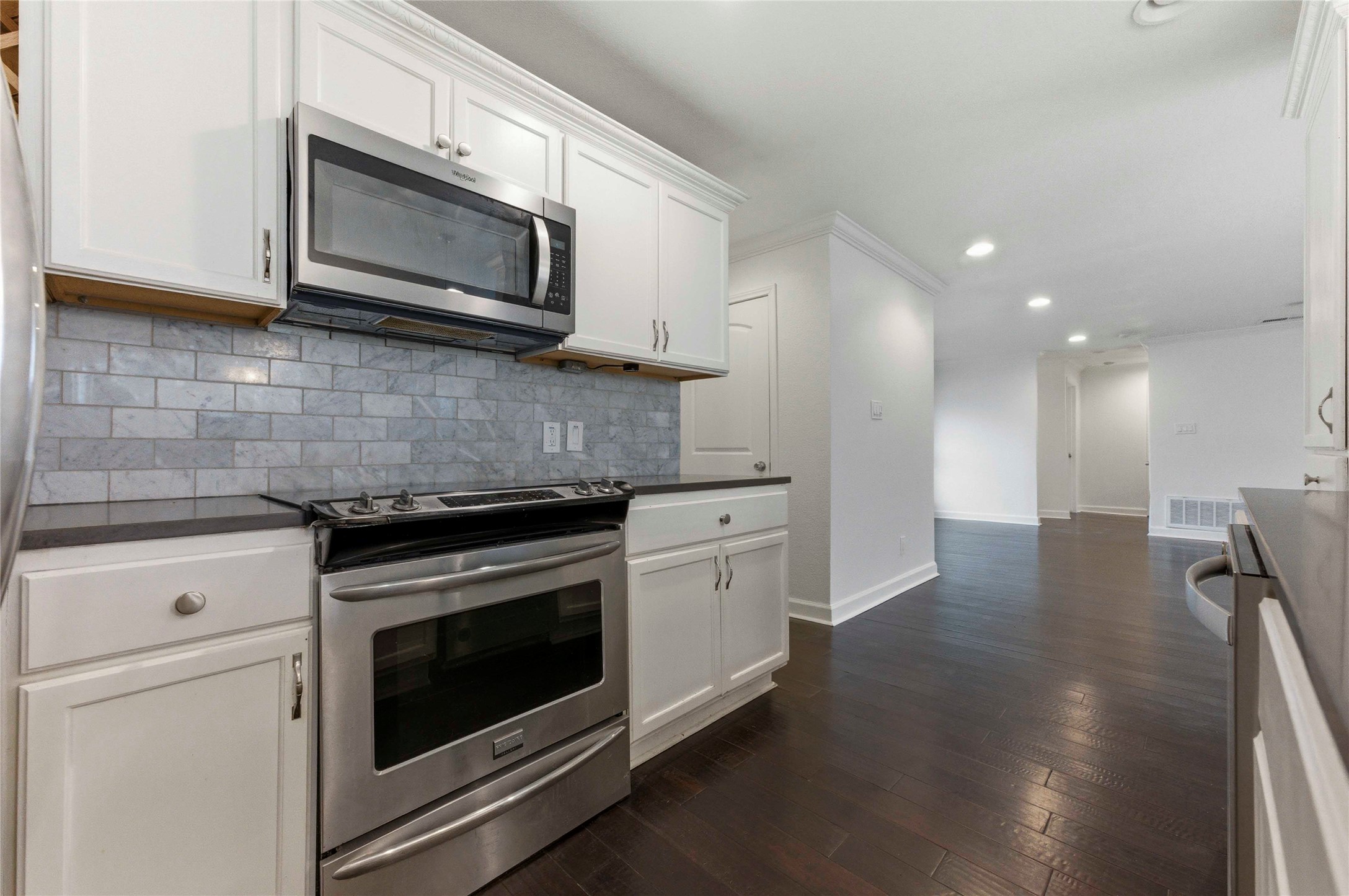 1909 Crooked Lane Austin, TX 78741 - Photo 10 of 25 Kitchen with stainless steel appliances, dark wood-type flooring, white cabinets, recessed lighting, and decorative backsplash