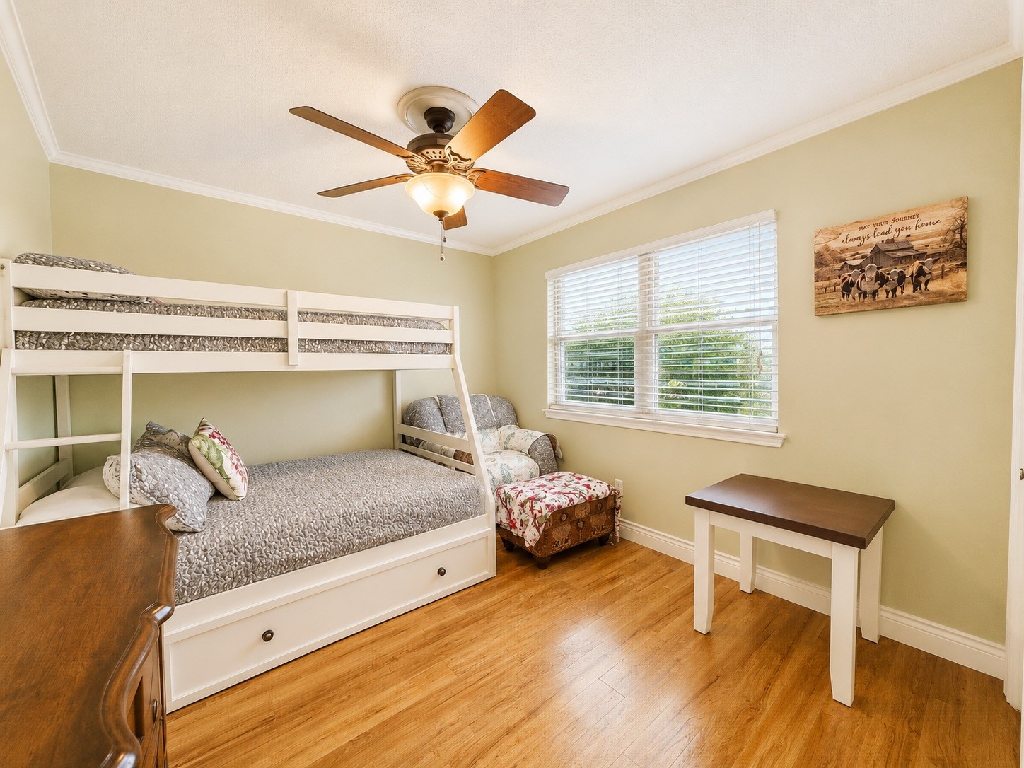 135 Sand Shoals Road Freeport, TX 77541 - Photo 15 of 20 This cozy bedroom features a bunk bed with a double bed on the bottom, a ceiling fan, and a large window for natural light. The room has warm wooden flooring and soft green walls, with additional seating and a small table for convenience.