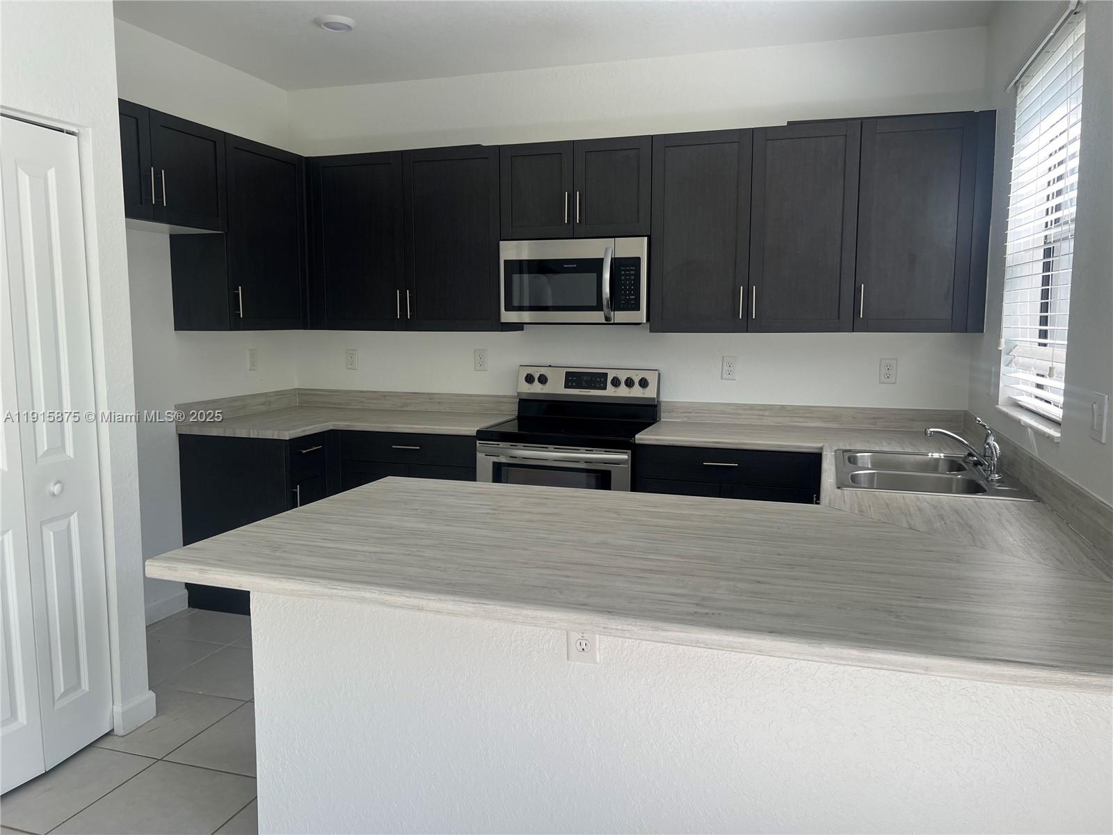 28701 Southwest 132nd Place Homestead, FL 33033 - Photo 7 of 17 a kitchen with stainless steel appliances a stove a microwave and white cabinets