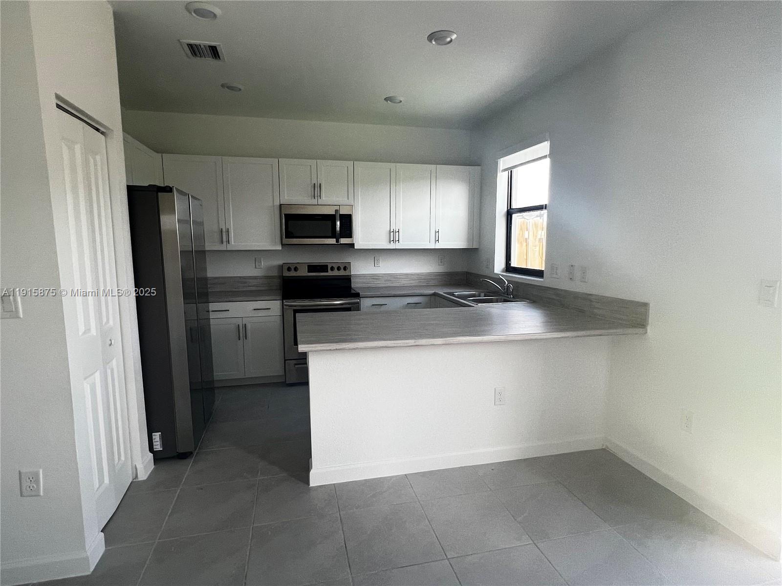 28701 Southwest 132nd Place Homestead, FL 33033 - Photo 9 of 17 a kitchen with stainless steel appliances granite countertop a refrigerator a stove a sink a microwave and white cabinets