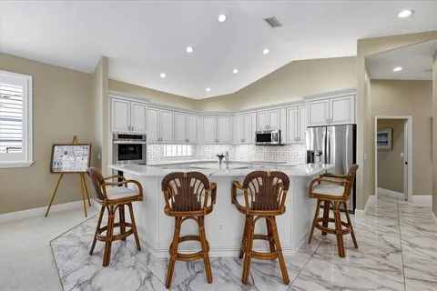 a kitchen with stainless steel appliances granite countertop a dining table chairs refrigerator and microwave