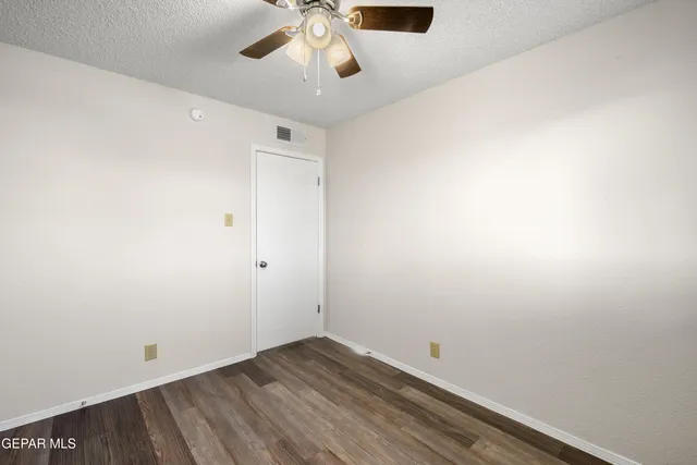 an empty room with a chandelier fan and wooden floor