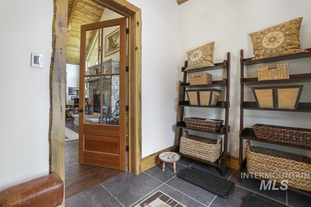 65 Goat Creek Way Stanley, ID 83278 - Photo 6 of 32 Entryway featuring large format tile flooring with an inlaid pattern, custom natural wood door casing, a clear-paneled wooden door, and visible vaulted wood-finish ceilings beyond