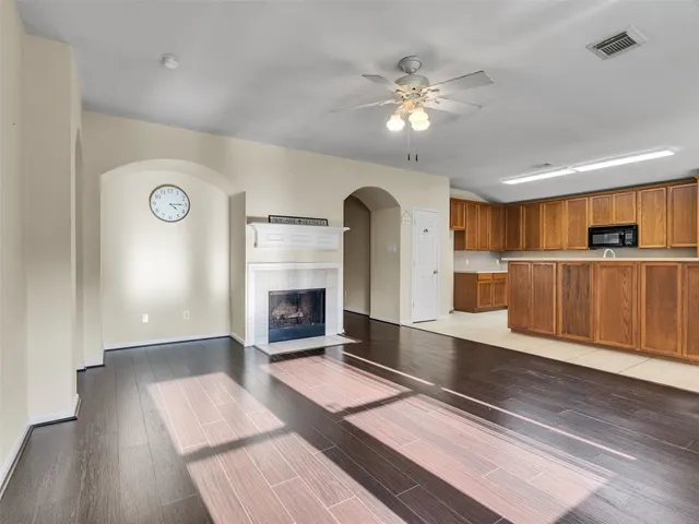 a view of an empty room with wooden floor and a kitchen