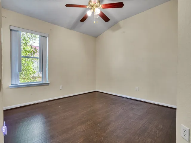 an empty room with wooden floor chandelier fan and windows