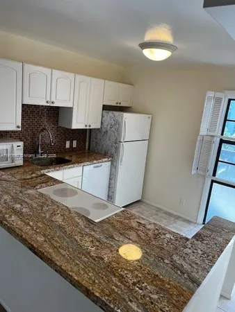 a kitchen with granite countertop a refrigerator a stove a sink and white cabinets