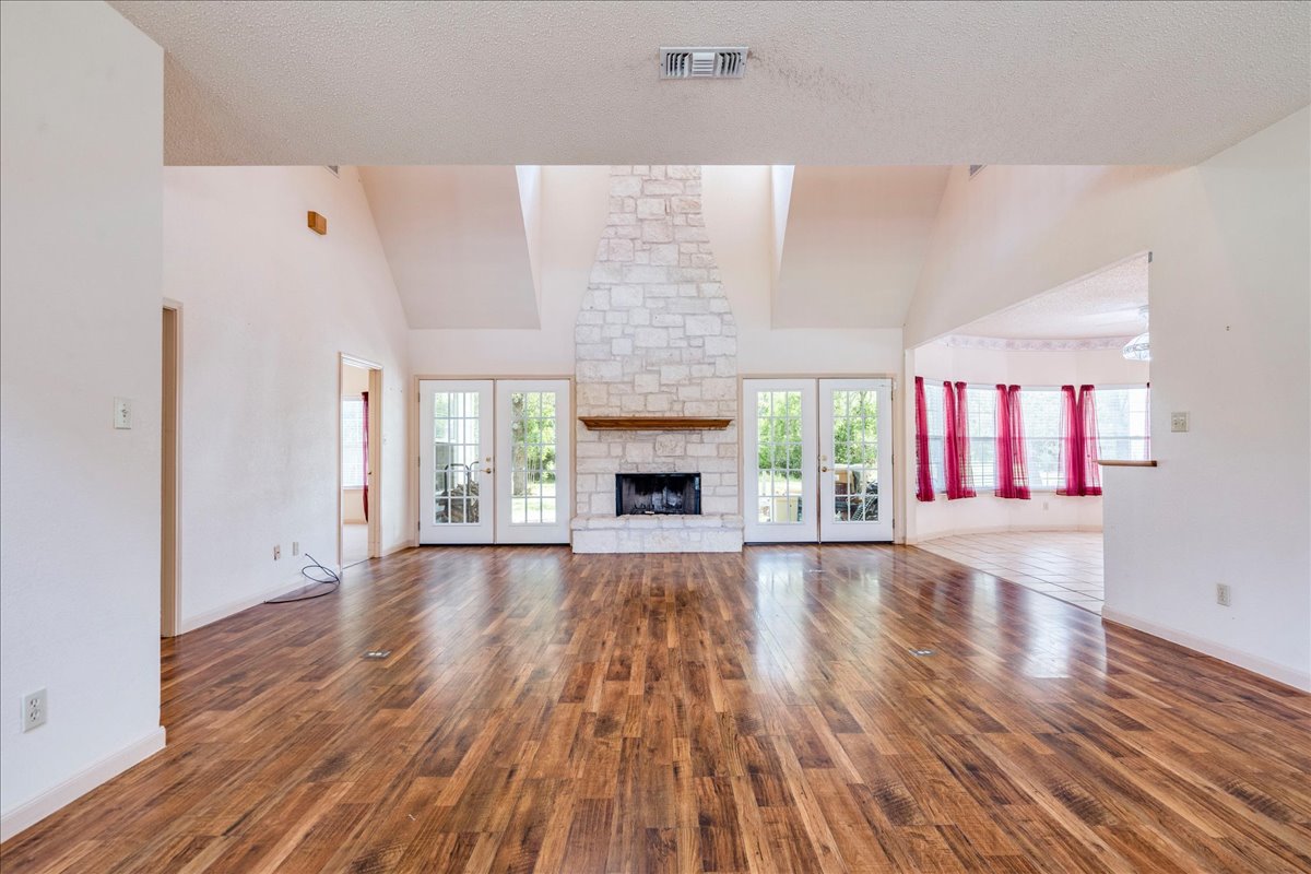 19106 Eyerley Road Manor, TX 78653 - Photo 7 of 40 A spacious living area showcases rich wood flooring, a striking stone fireplace, and French doors opening to outdoor serenity.