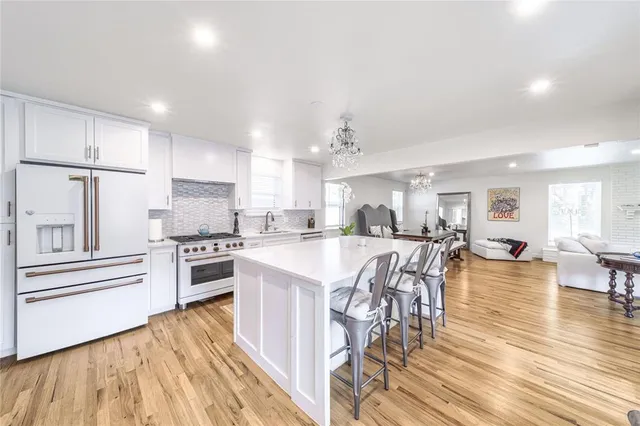 a kitchen with stainless steel appliances kitchen island granite countertop a stove a refrigerator a dining table and chairs with wooden floor