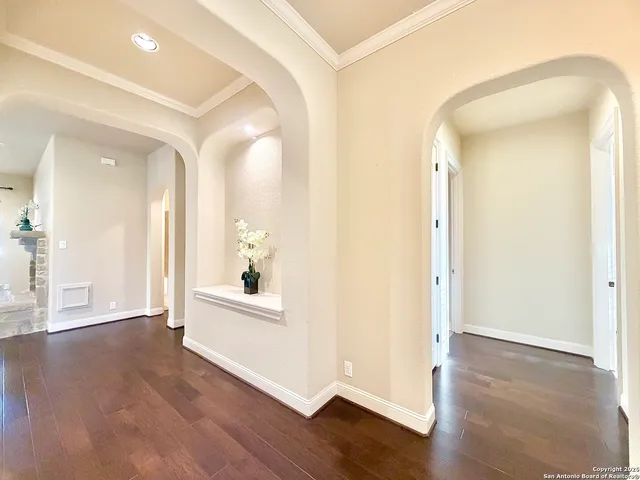 a view of a hallway to an empty room with wooden floor and a bathroom