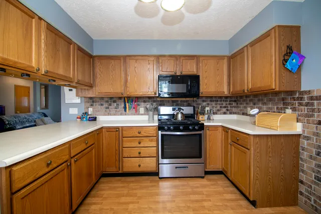 a kitchen with stainless steel appliances granite countertop a stove top oven a sink dishwasher and a refrigerator with wooden cabinets