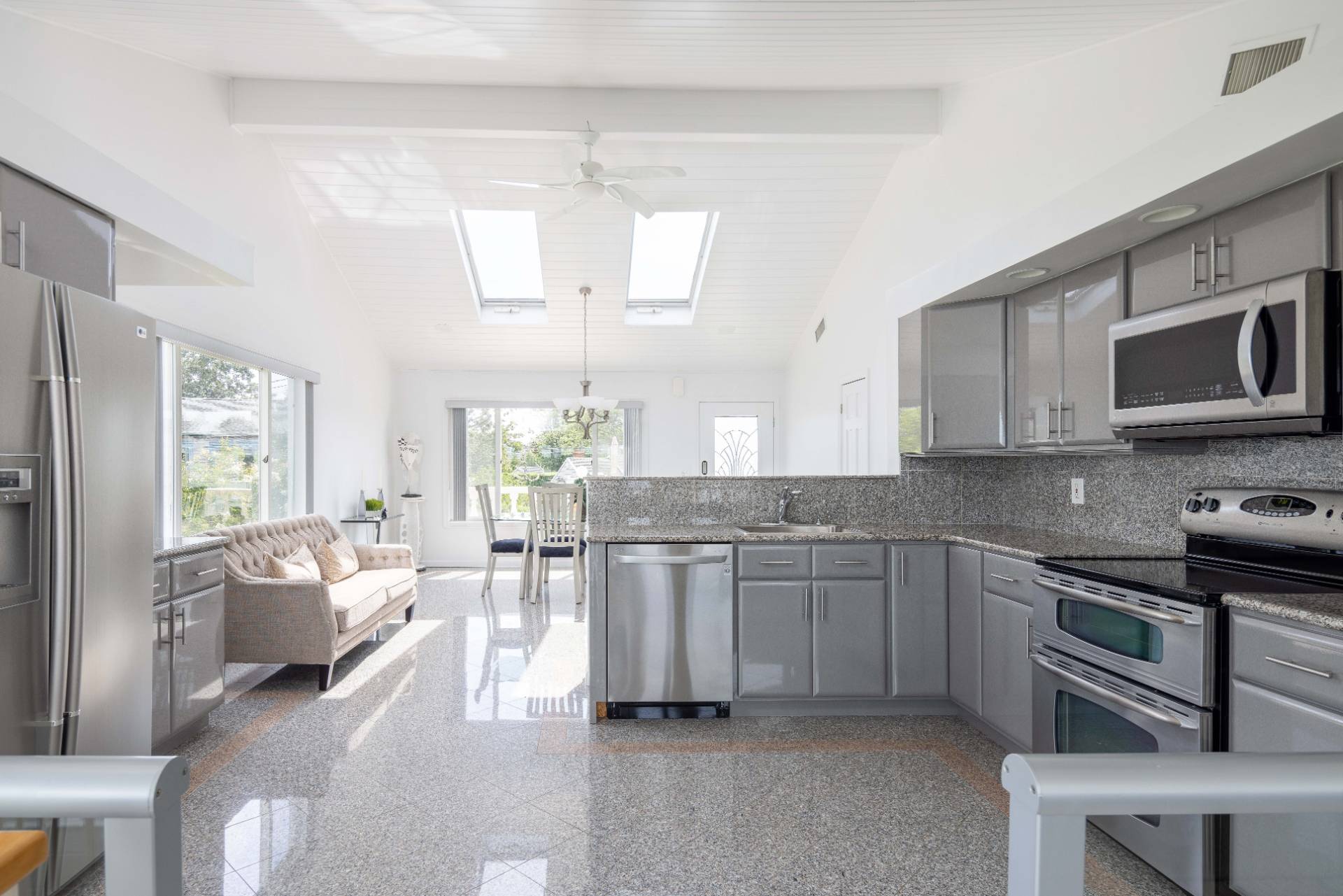 69 B Little Pine Lane East Quogue, NY 11942 - Photo 4 of 34 a kitchen with stainless steel appliances granite countertop a stove top oven a sink dishwasher a dining table and chairs with wooden floor
