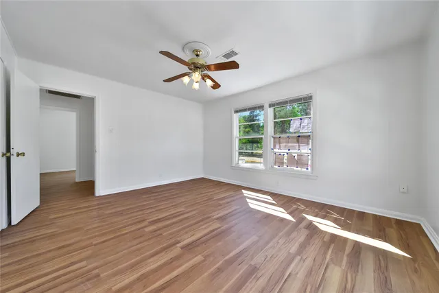 an empty room with wooden floor fan and windows