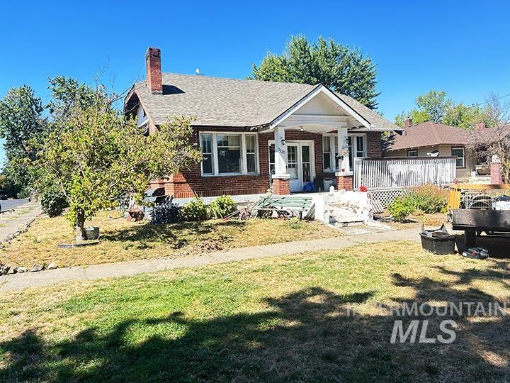 Bungalow-style home featuring brick siding, a chimney, a front lawn, covered porch, and roof with shingles