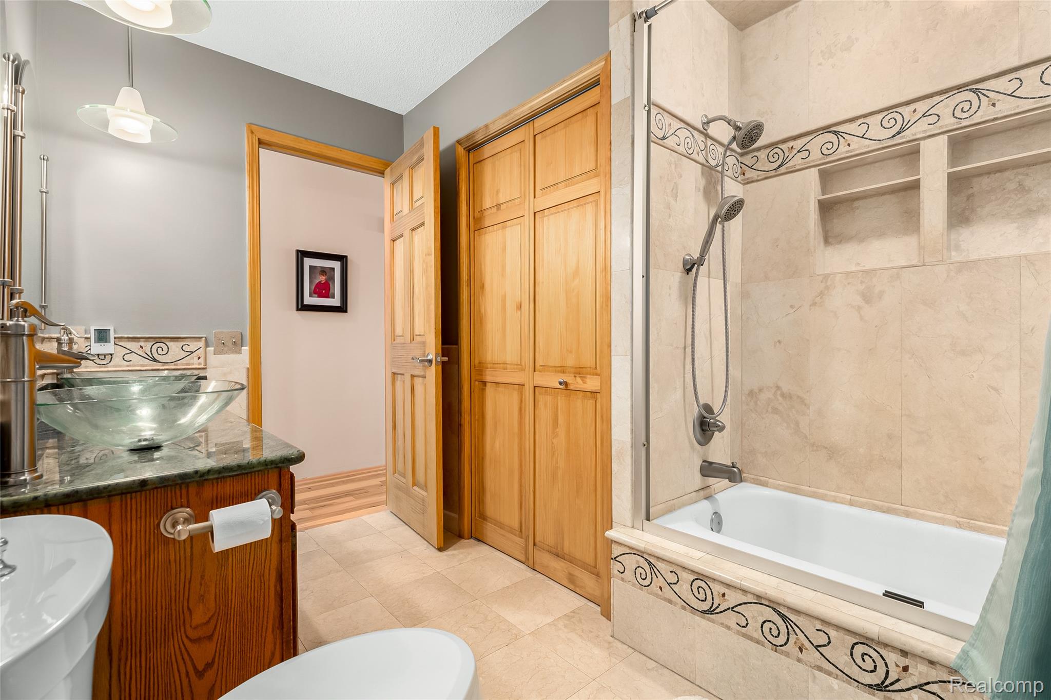 15395 Osius Road Chelsea, MI 48118 - Photo 19 of 55 Bathroom featuring a vessel sink with a stone countertop vanity, an integrated bathtub and shower combination with a tiled surround, and natural wood doors