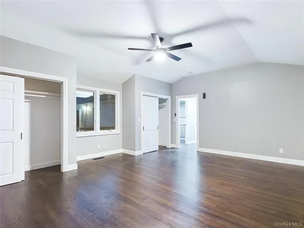 a view of an empty room with wooden floor and a ceiling fan