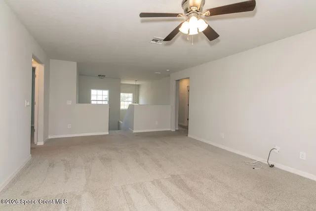 an empty room with chandelier fan and windows